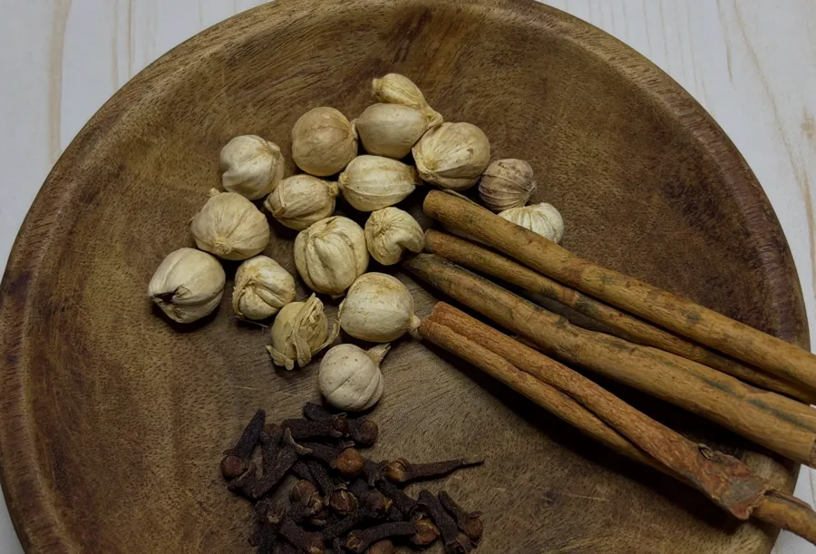 Green cardamom, cinnamon sticks and cloves on a wooden plate